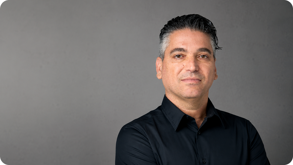Head-and-shoulders portrait of a man in a black button-down shirt against a gray studio backdrop.
