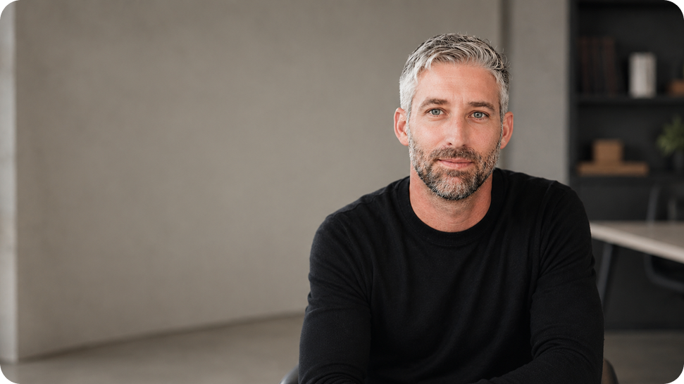 Portrait of a middle-aged man with gray hair and beard wearing a black sweater, seated indoors at a desk.